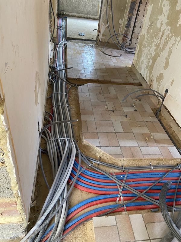 Faisceau de gaines électriques posé au sol d’un couloir en rénovation